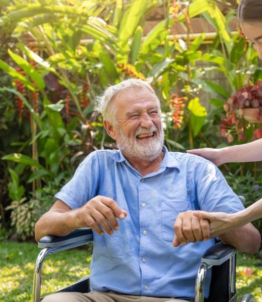 Happy nurse holding laughing elderly man hand on wheelchair in garden at nursing home