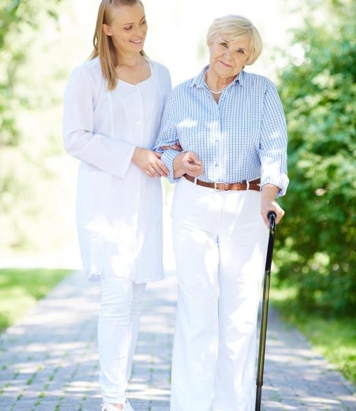 Pretty nurse and senior patient with walking stick having a walk in park
