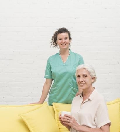 smiling-senior-woman-sitting-sofa-holding-coffee-cup-front-nurse